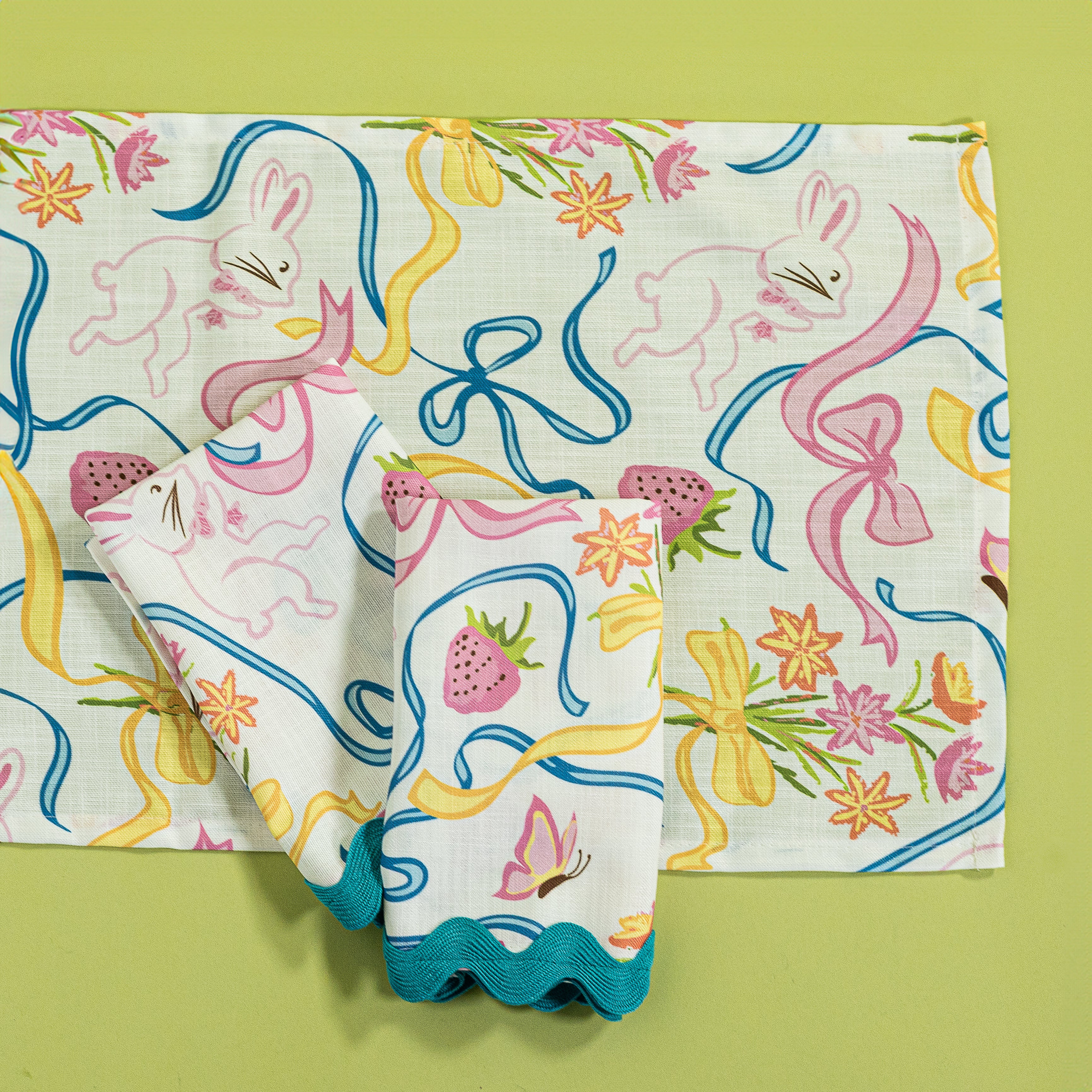 A Bunnies and bow print fabric napkins and table runner in multicolor against a light green background.