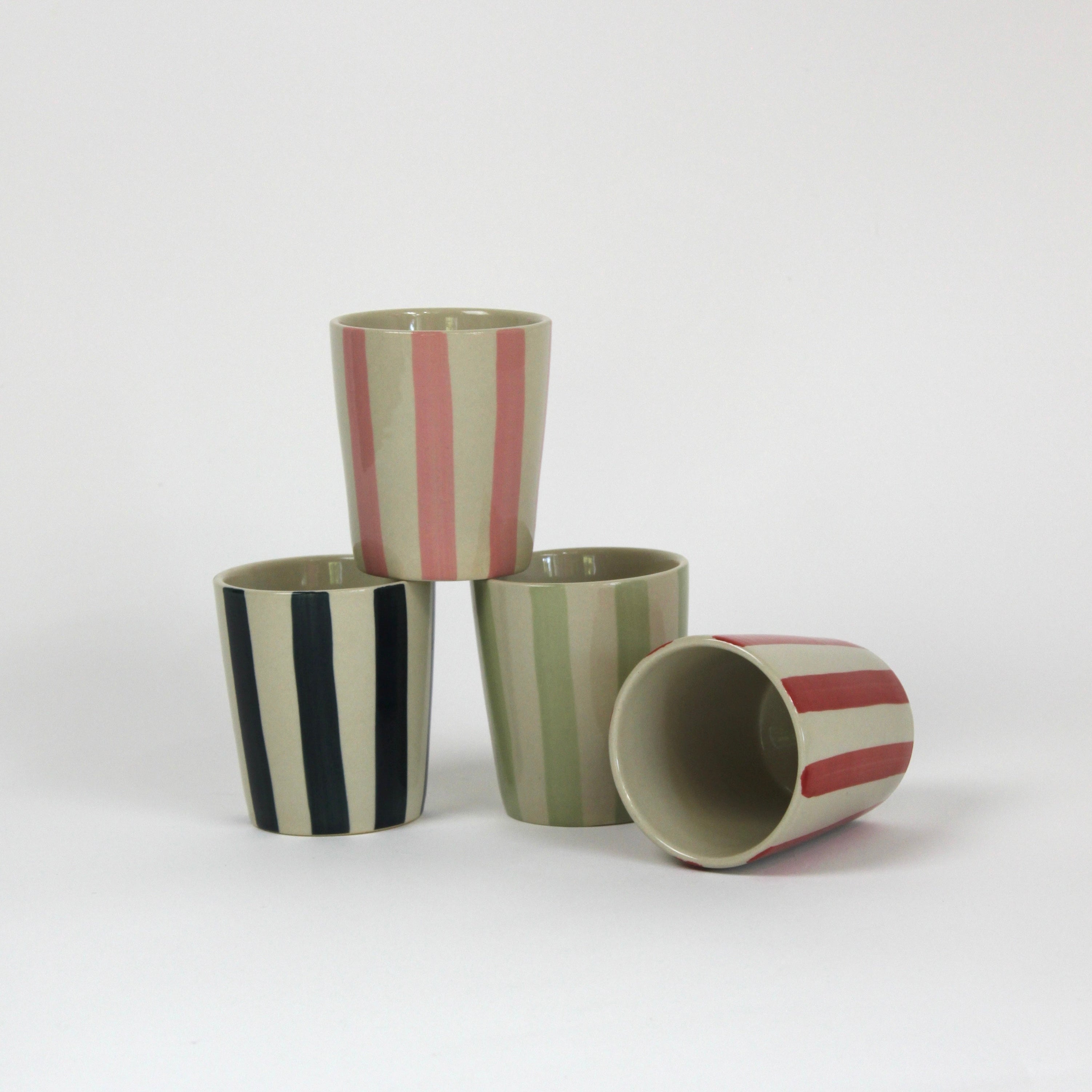set of 4 Hand-Painted Striped Ceramic Cups in different colors, red, blue, green and pink in a white background. the red is laid and showing the inside of cup.