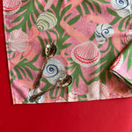 Open, flat Shell Seekers pink and green cloth dinner napkins with a shell and seaweed pattern
