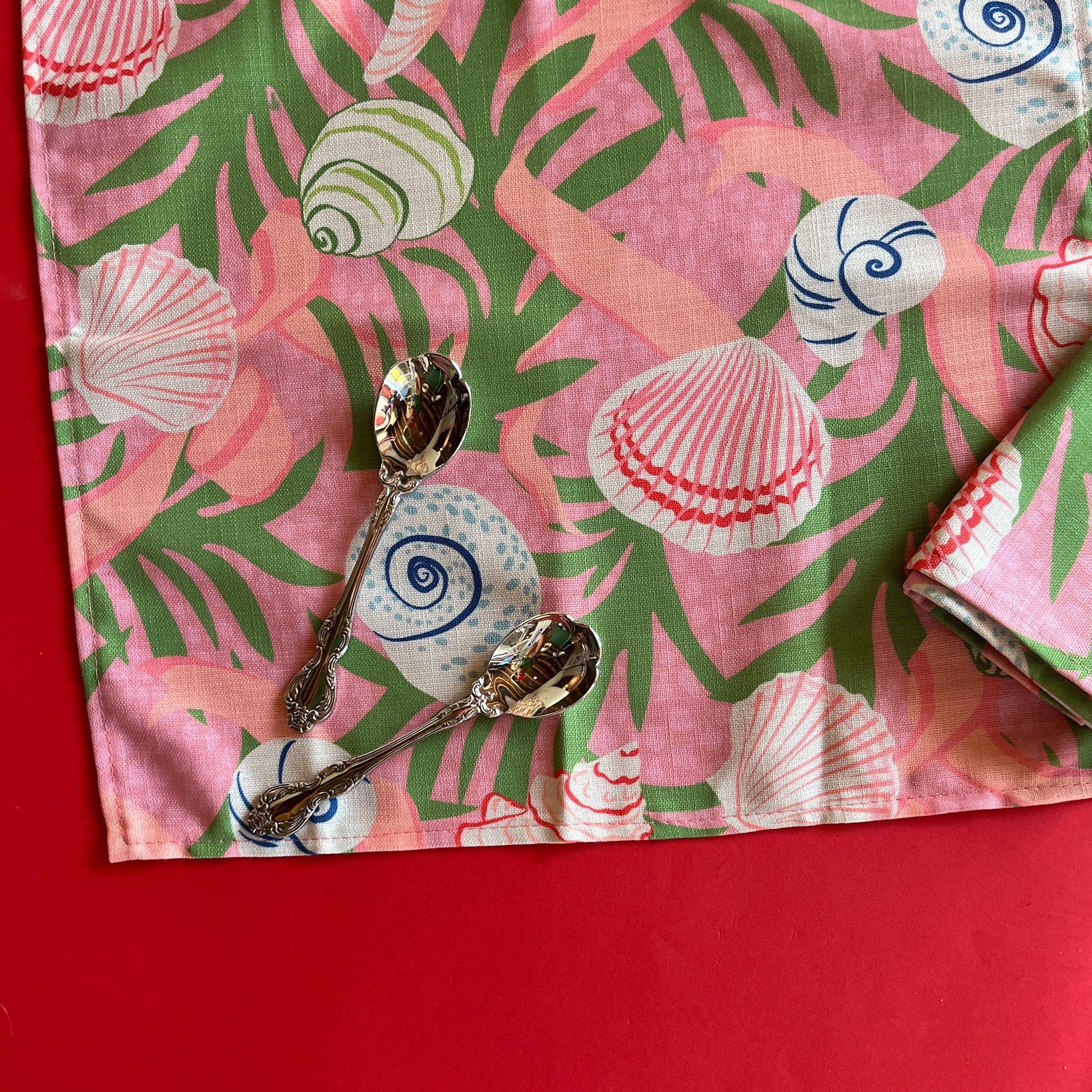Open, flat Shell Seekers pink and green cloth dinner napkins with a shell and seaweed pattern