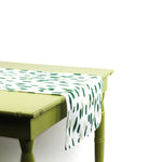 Side view of green and white brushstroke dot table runner draped over the edge of a light green table.
