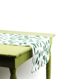 Side view of green and white brushstroke dot table runner draped over the edge of a light green table.