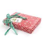 Red geometric wrapping paper displayed wrapped on a flat gift with green ribbon.