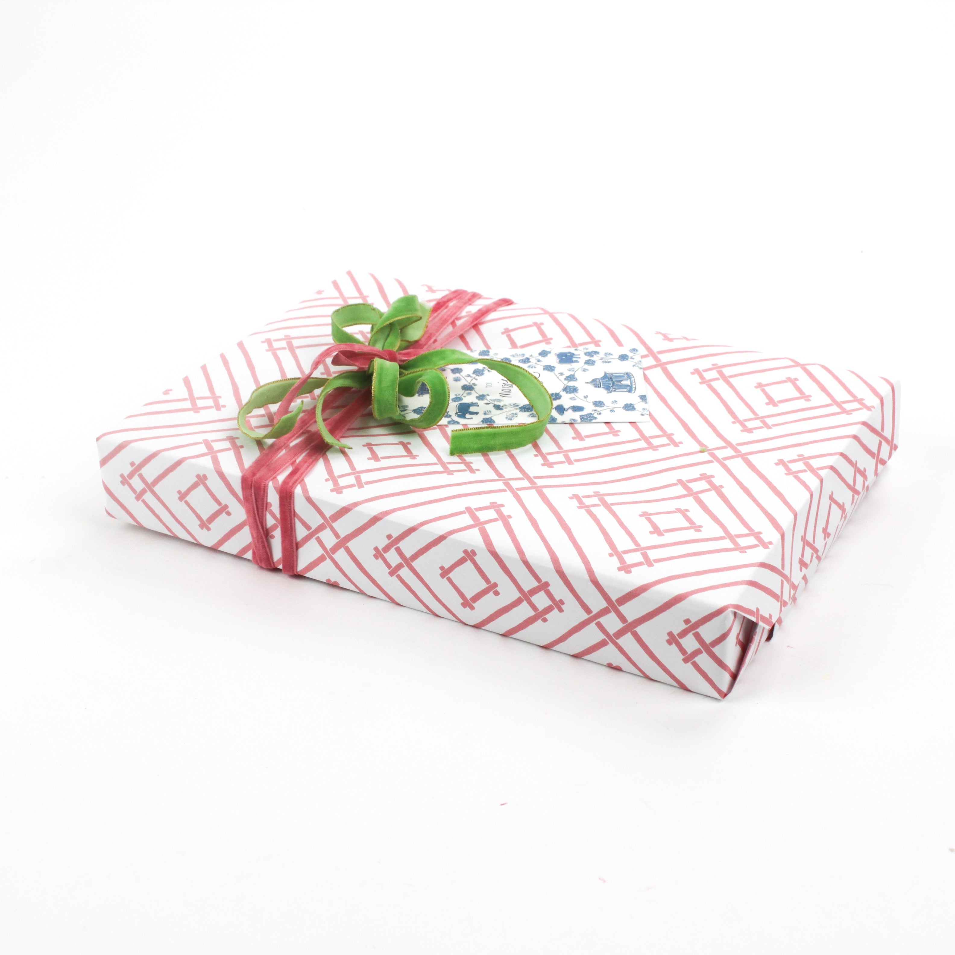 Gift box wrapped in red and white geometric patterned paper with green and red ribbon and a decorative gift tag.