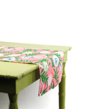 Close-up angled view of a pink and green table runner with seashell designs draped over a green table.