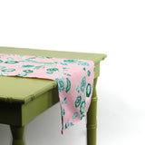 Side view of a pink floral table runner draped over a green table.