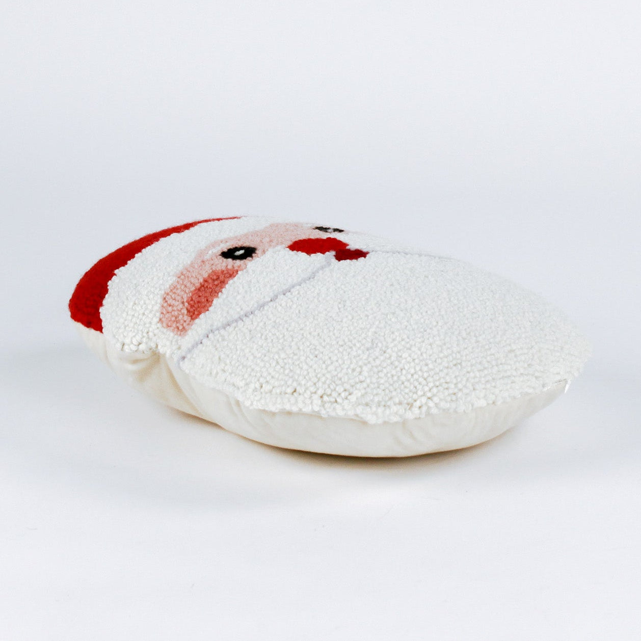 side of a Santa-shaped christmas pillow with a hooked texture, featuring Santa’s face with rosy cheeks, a red nose, and a bright red hat with a white pom-pom.