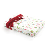 Side view of gift wrapped in Christmas ornament print paper with red ribbon and tag.