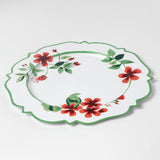 A white tole metal floral charger plate decorated with red geraniums with a green border against a white background. 