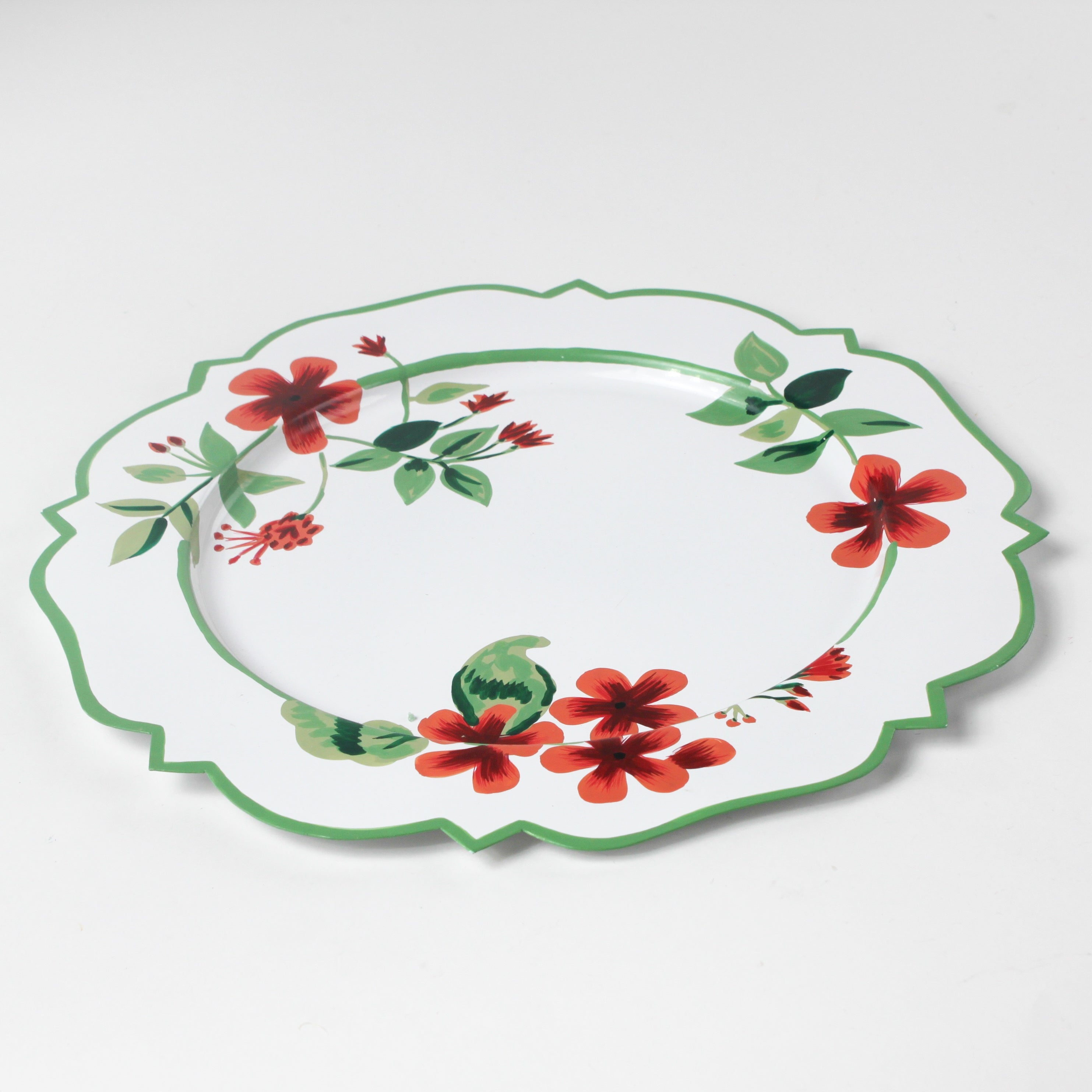 A white tole metal floral charger plate decorated with red geraniums with a green border against a white background. 
