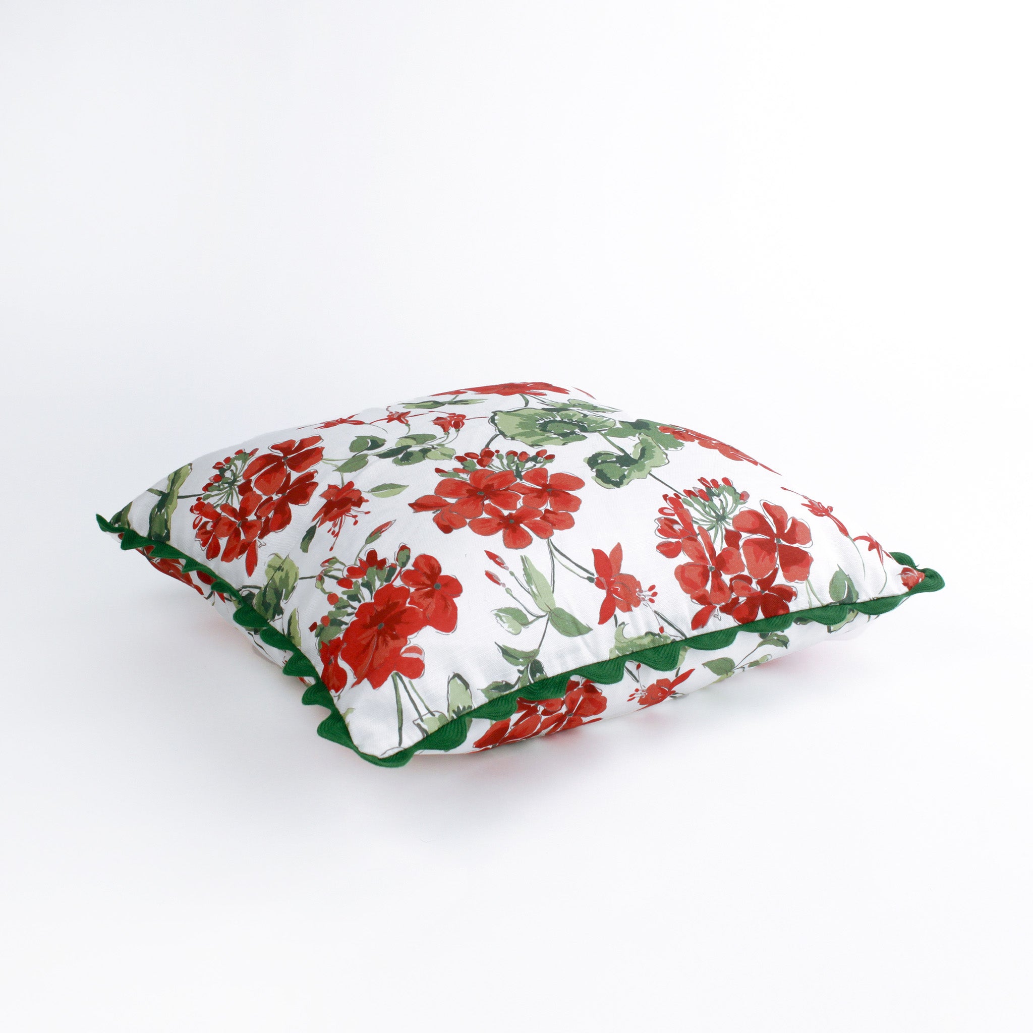 Square decorative pillow featuring a red and green floral geranium pattern on a white background, finished with a dark green scalloped trim around the edges.