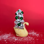 A yellow coloured Vintage Distressed Ceramic Swan centerpiece with a Flocked Christmas Tree inside it against a red background. 