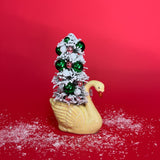 A yellow coloured Vintage Distressed Ceramic Swan centerpiece with a Flocked Christmas Tree inside it against a red background. 