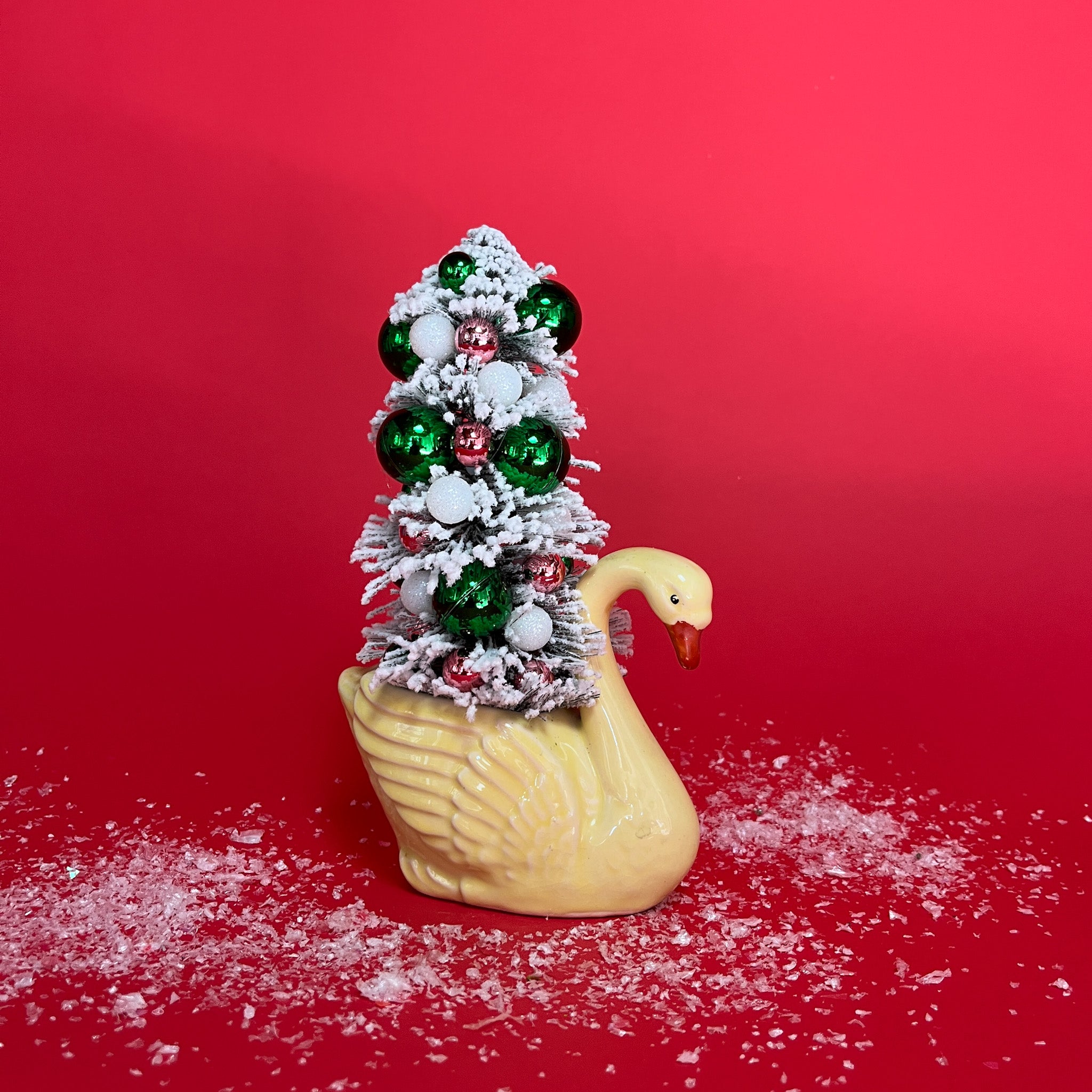 A yellow coloured Vintage Distressed White Ceramic Swan centerpiece with a Flocked Christmas Tree inside it against a red background. 