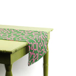 Close-up angled view of a green and pink patterned table runner draped over a light green table.