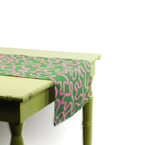 Close-up angled view of a green and pink patterned table runner draped over a light green table.