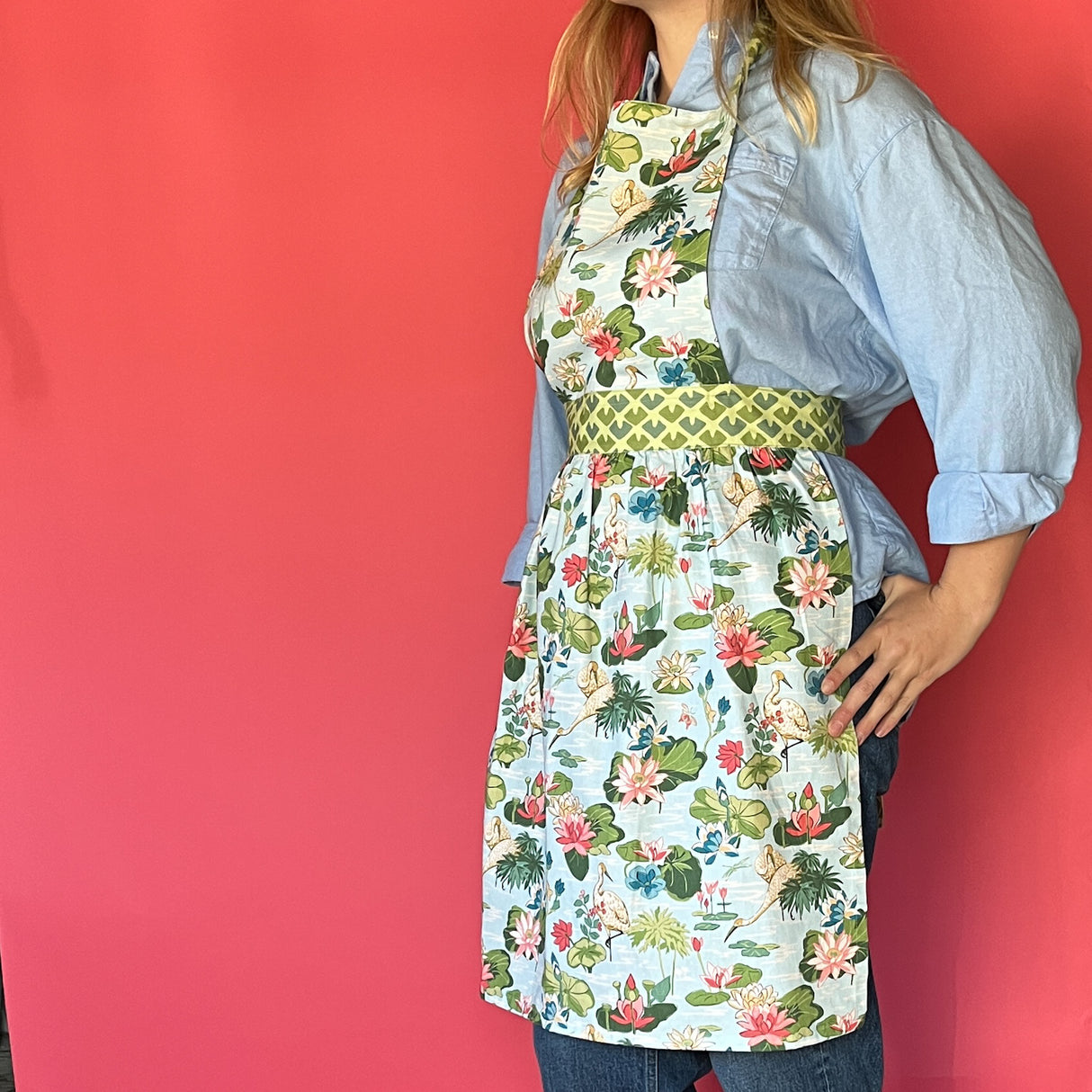 a woman wearing a green, pink and blue floral apron featuring the Meadow bluc water lilies pattern fabric from madcap cottage