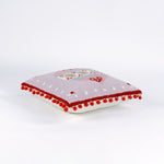 Pink Christmas pillow with red pom-pom trim and a large central ornament motif