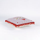 Pink Christmas pillow with red pom-pom trim and a large central ornament motif