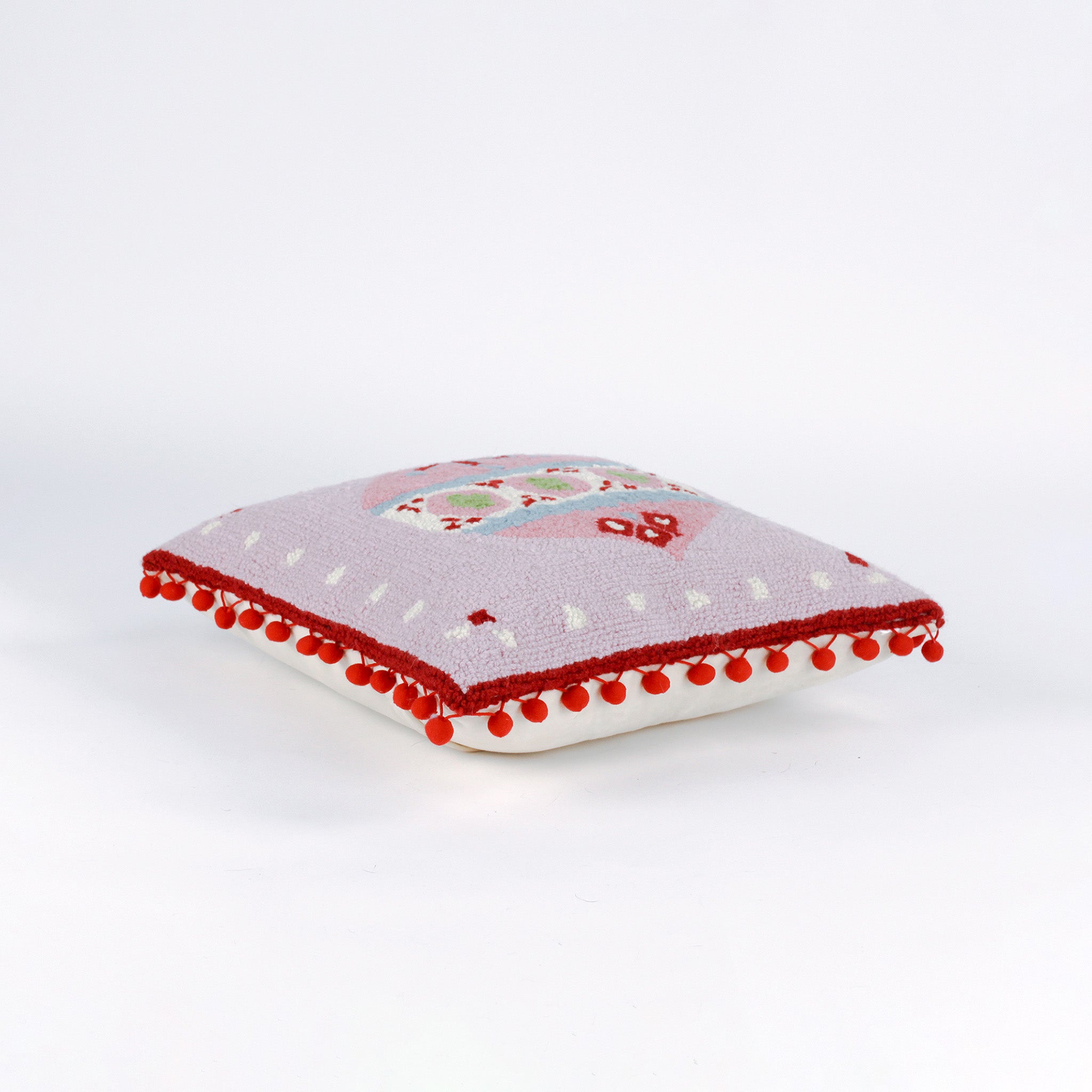 Pink Christmas pillow with red pom-pom trim and a large central ornament motif