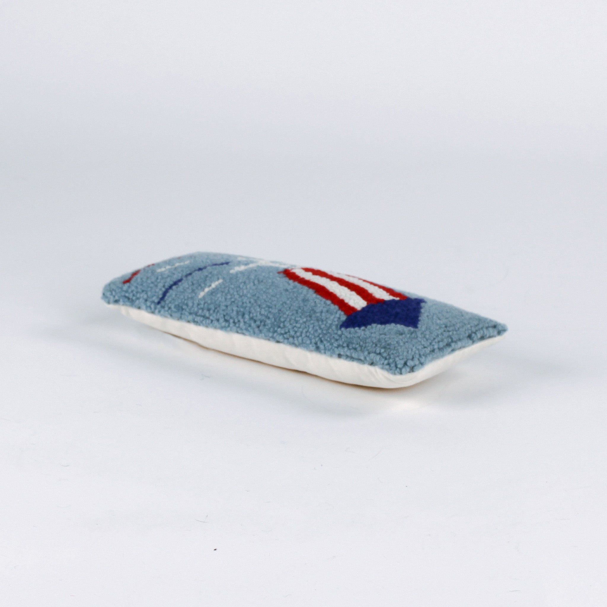 Rectangular blue decorative pillow with a hooked texture featuring a red, white, and blue fireworks rocket design, shown on a white background.