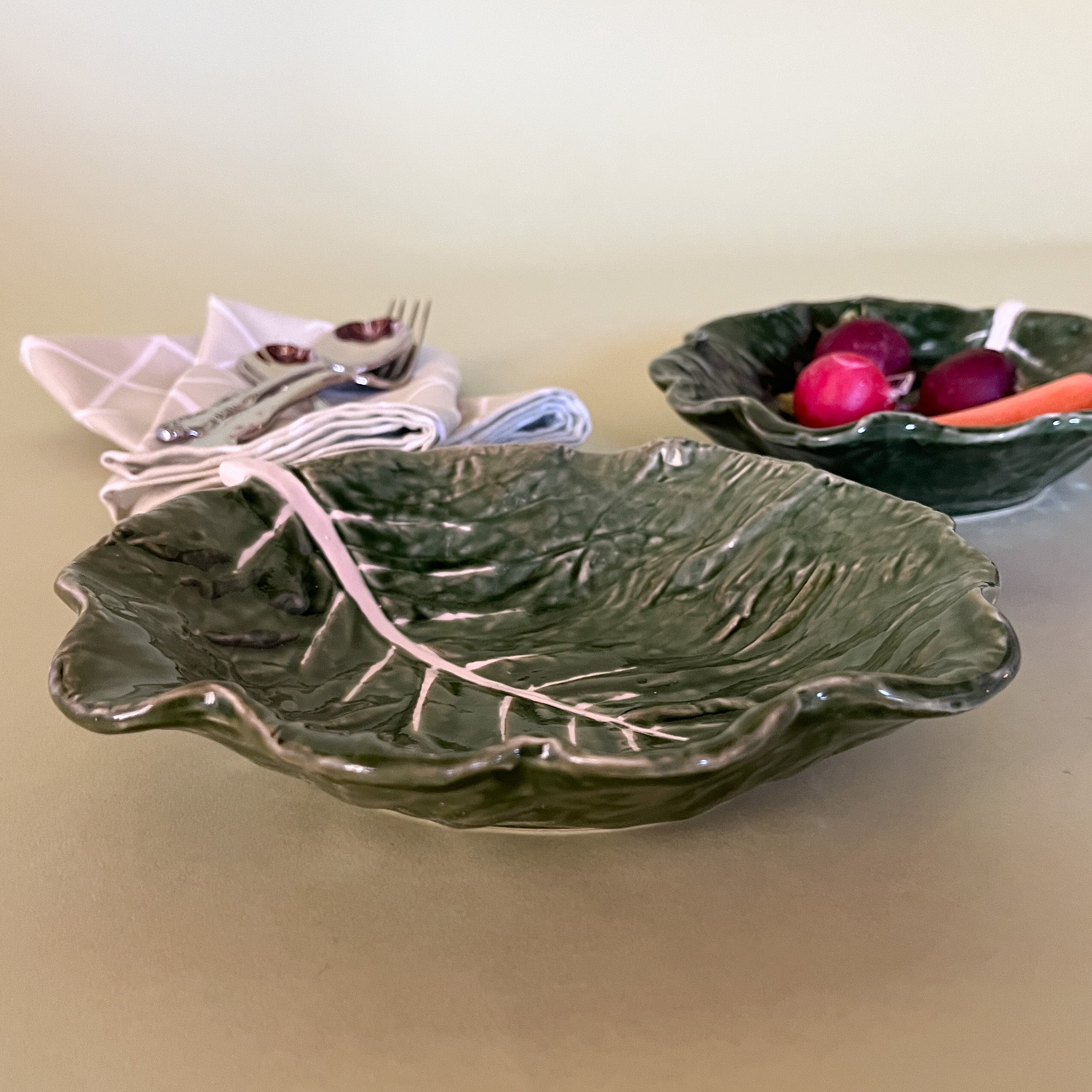 the side view of two ceramic cabbage leaf bowls one filled with radishes.