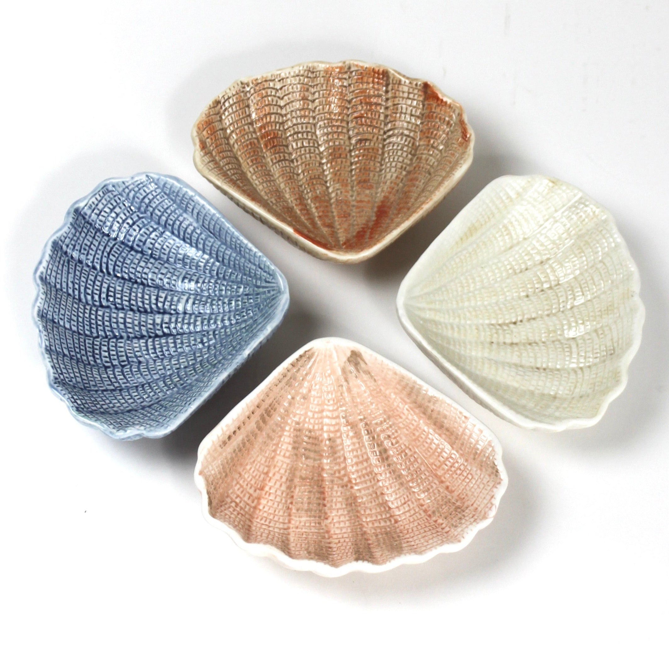 a small ceramic shell bowl set featuring four shells in blue, brown, pink and white