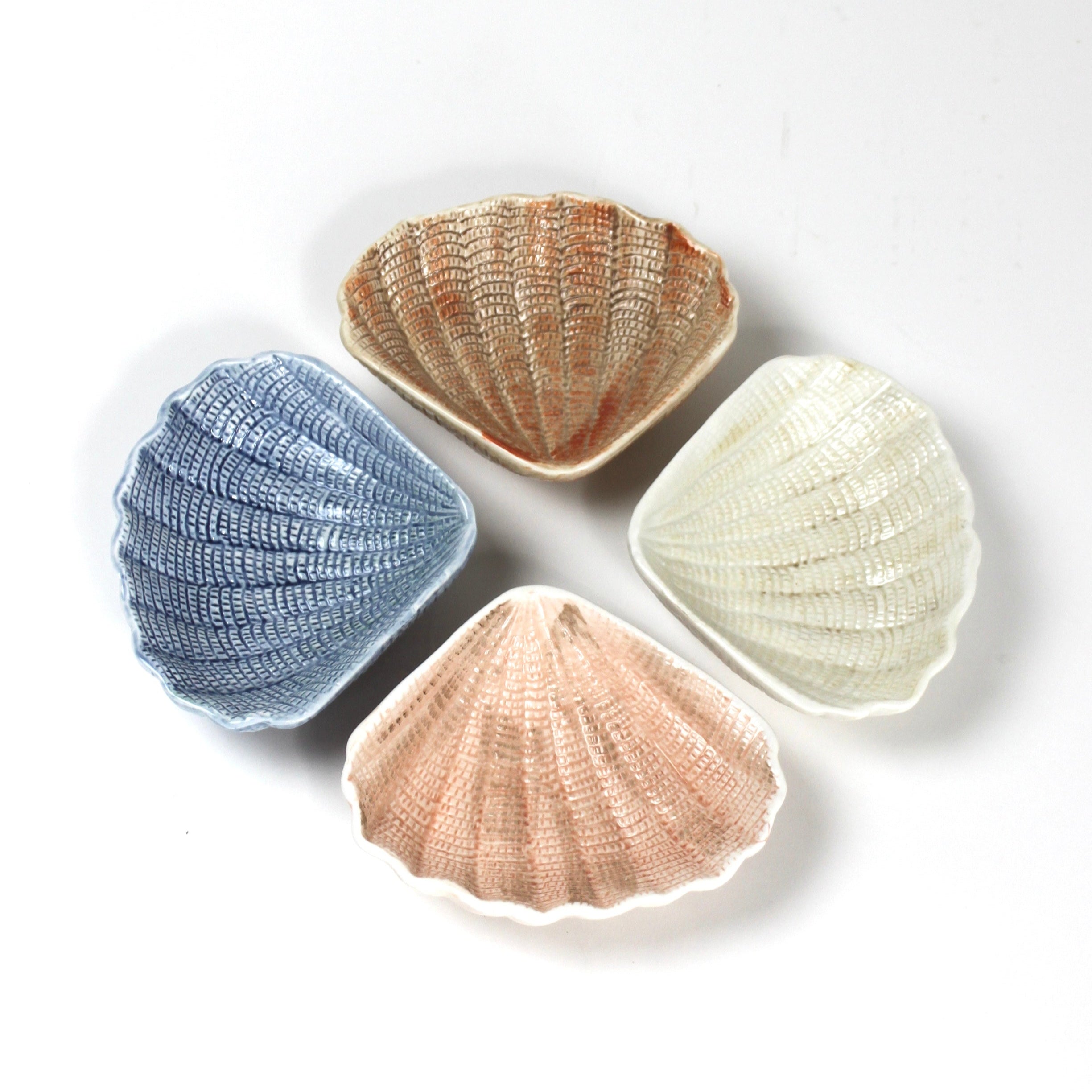 a small ceramic shell bowl set featuring four shells in blue, brown, pink and white