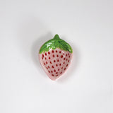 a small pink strawberry shaped bowl painted to look like a strawberry resting on a white background
