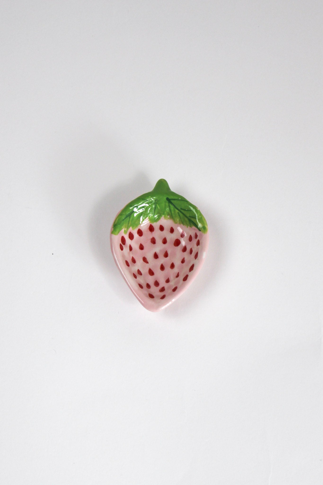 a small pink strawberry shaped bowl painted to look like a strawberry resting on a white background