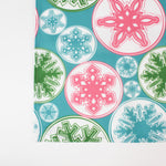 a blue christmas table runner with a pink, green and blue snowflake motif pattern against a white background. 