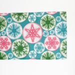 a blue christmas table runner with a pink, green and blue snowflake motif pattern against a white background. 