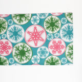 a blue christmas table runner with a pink, green and blue snowflake motif pattern against a white background. 