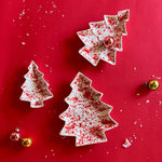 three christmas tree shaped vintage plates with a white glaze and red splatter effect paint on a red background. 