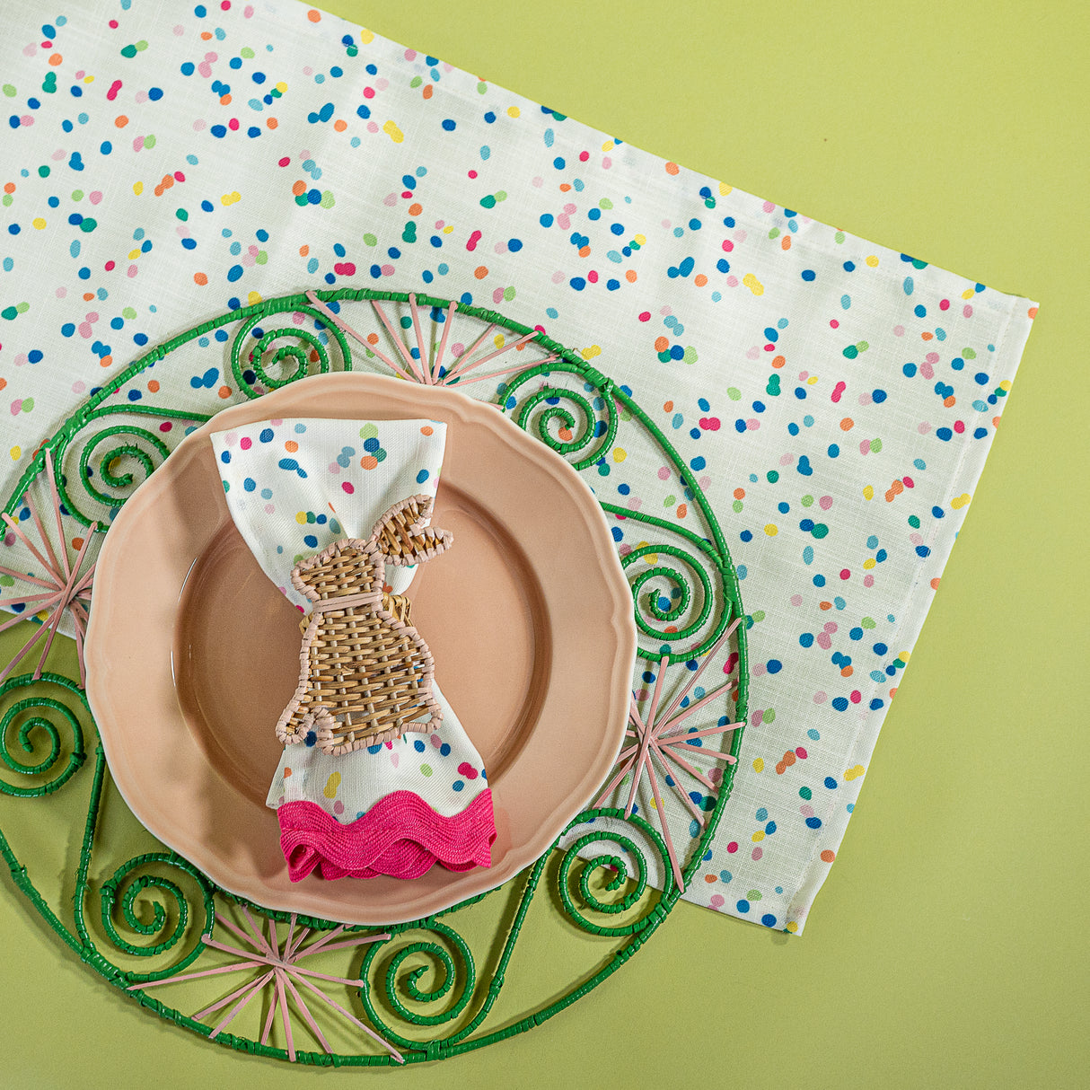 A Springtime confetti print cloth table runner with a pink plate and napkin on top