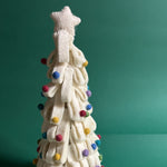 a white Looped Felt Christmas Tree Table Decoration with colourful bauble decorations, topped with a star against a green, snow scattered background. 