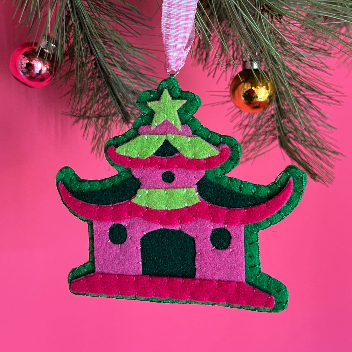 pink felt chinoiserie christmas ornaments in the shape of pagodas against a red background 