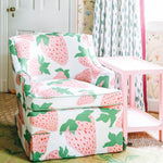 a chair upholstered in strawberry fabric with large pink strawberries next to a pink side table from madcap cottage