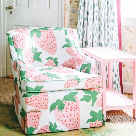 a chair upholstered in strawberry fabric with large pink strawberries next to a pink side table from madcap cottage