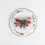 Lifestyle shot of the cottage grove geranium red floral plate with a white plate resting on it, holding a napkin with rattan ribbon napkin ring.