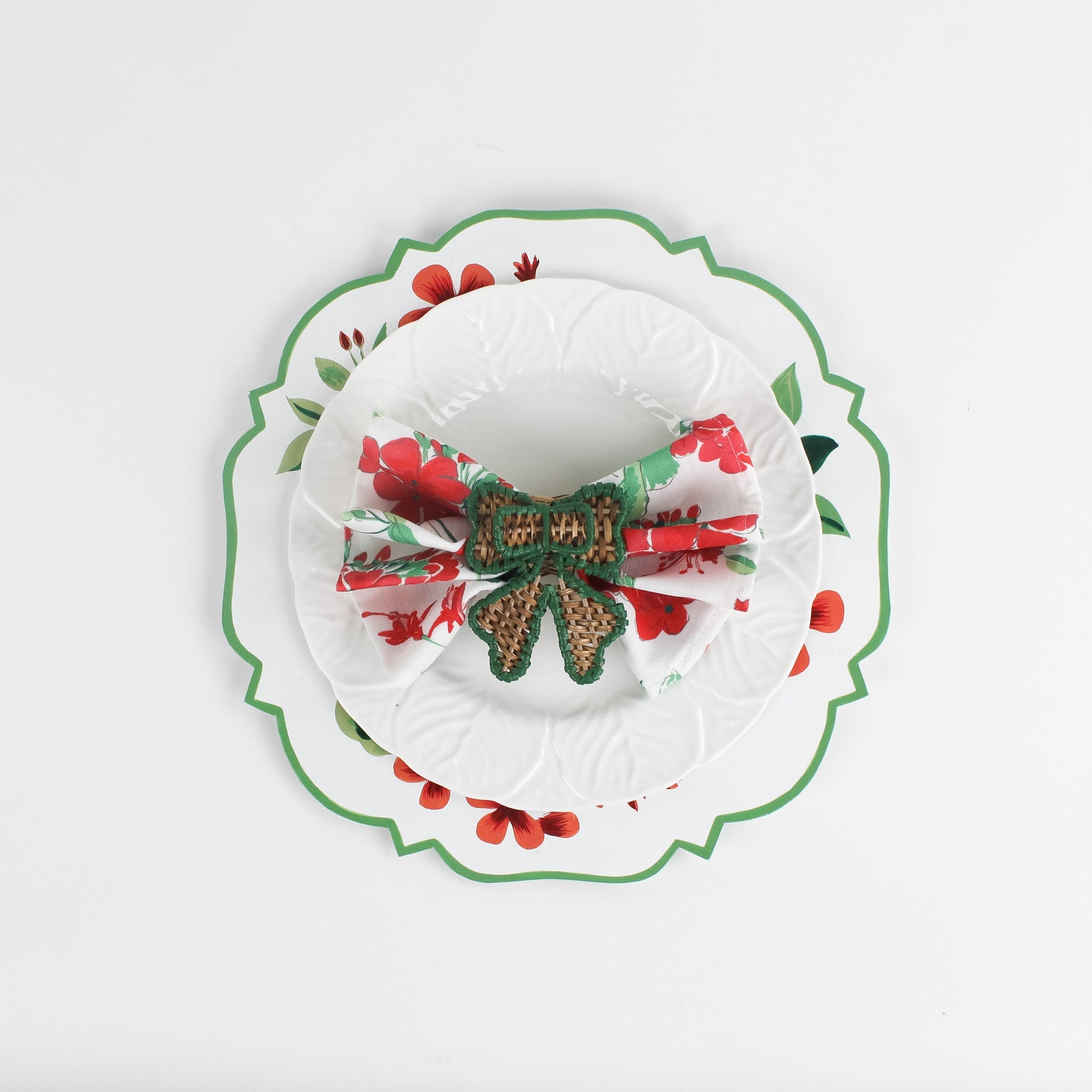 Lifestyle shot of the cottage grove geranium red floral plate with a white plate resting on it, holding a napkin with rattan ribbon napkin ring.
