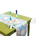 Styled blue patterned table runner on a green table with candles and a ribbon accent.