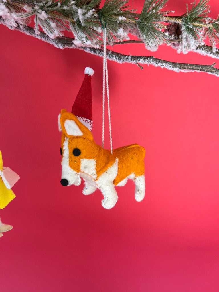 Corgi Christmas ornament with a Santa hat hanging from a tree branch against a red background