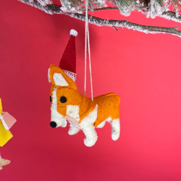 Corgi Christmas ornament with a Santa hat hanging from a tree branch against a red background