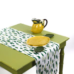 Green and white brushstroke dot table runner styled with a yellow lemon pitcher and matching serving dish on a light green table.