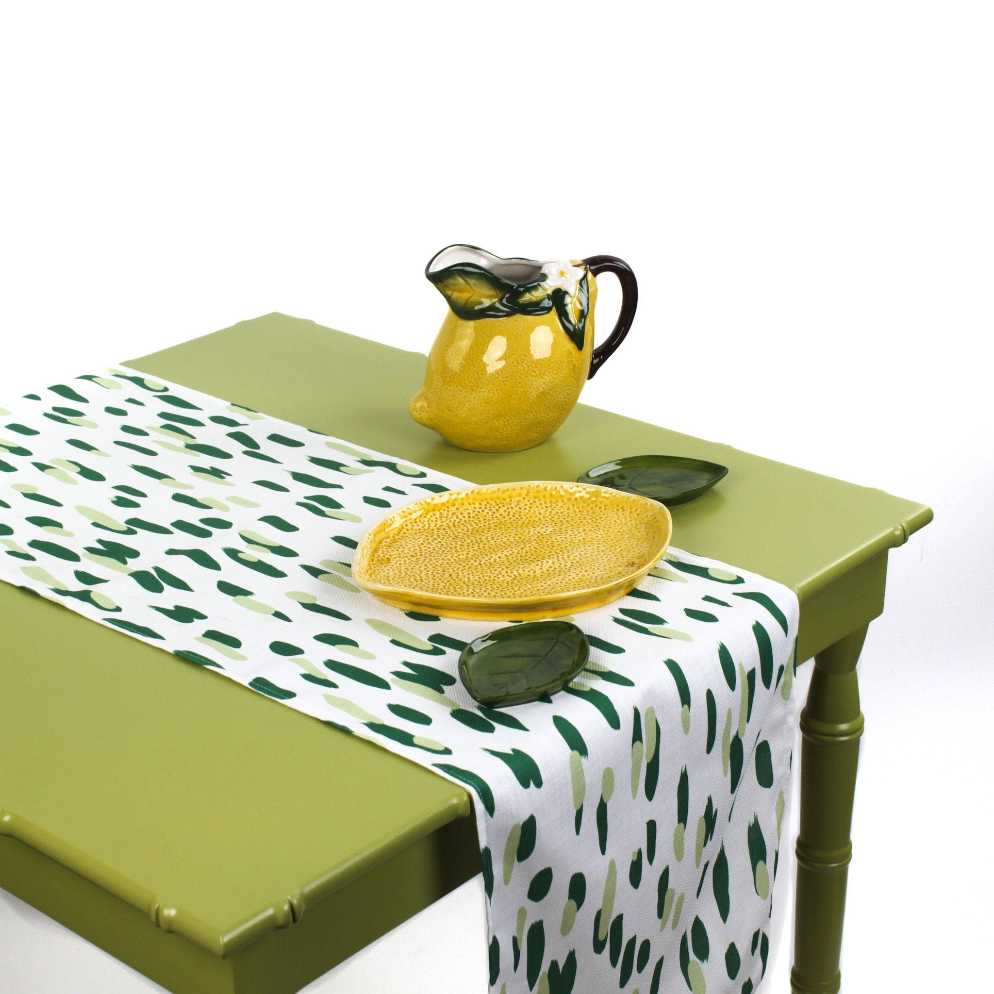 Green and white brushstroke dot table runner styled with a yellow lemon pitcher and matching serving dish on a light green table.