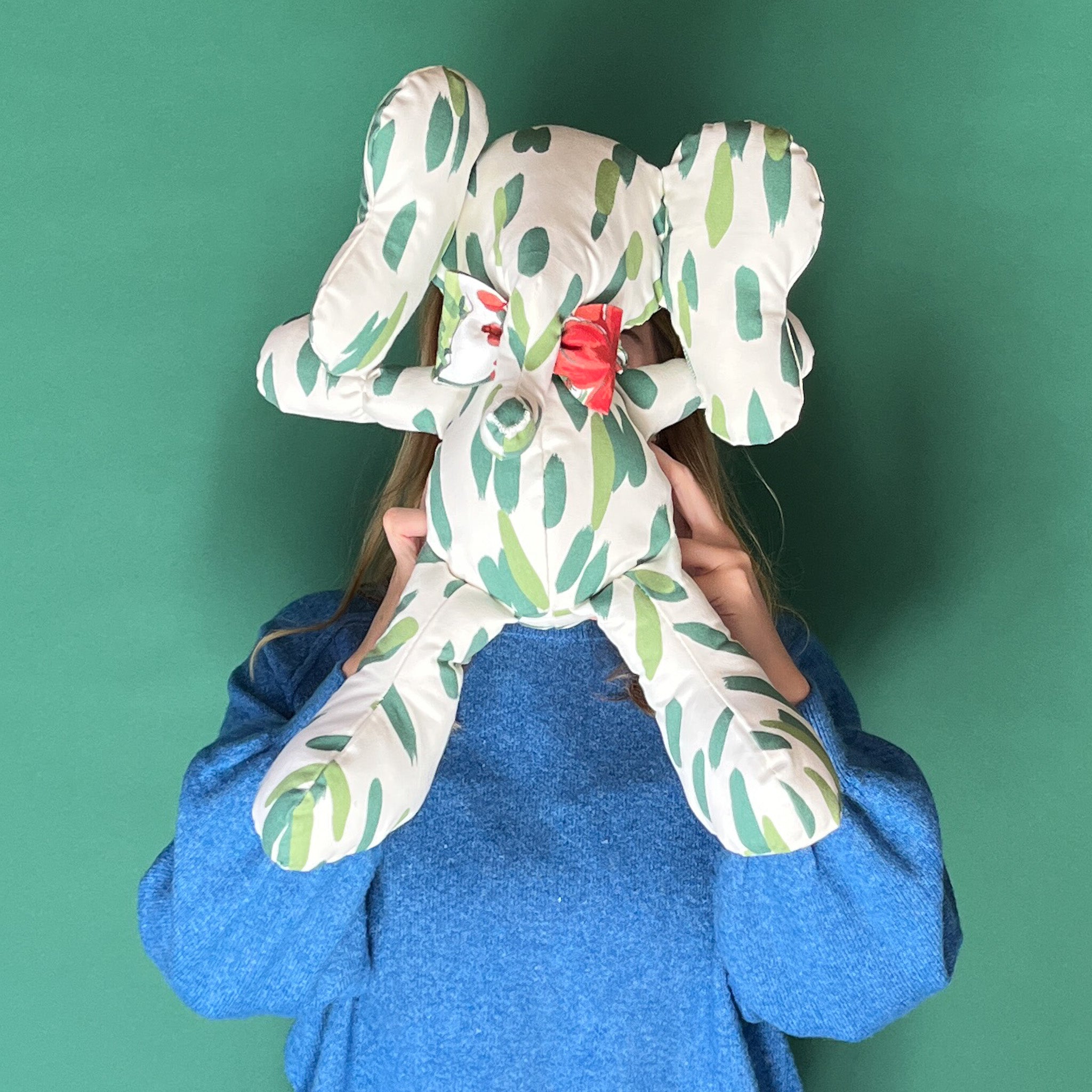 a Club House palm Green Stuffed Elephant held by a lady on a green background