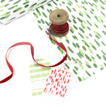 Styled display of green brushstroke wrapping paper with gift tags and red ribbon.