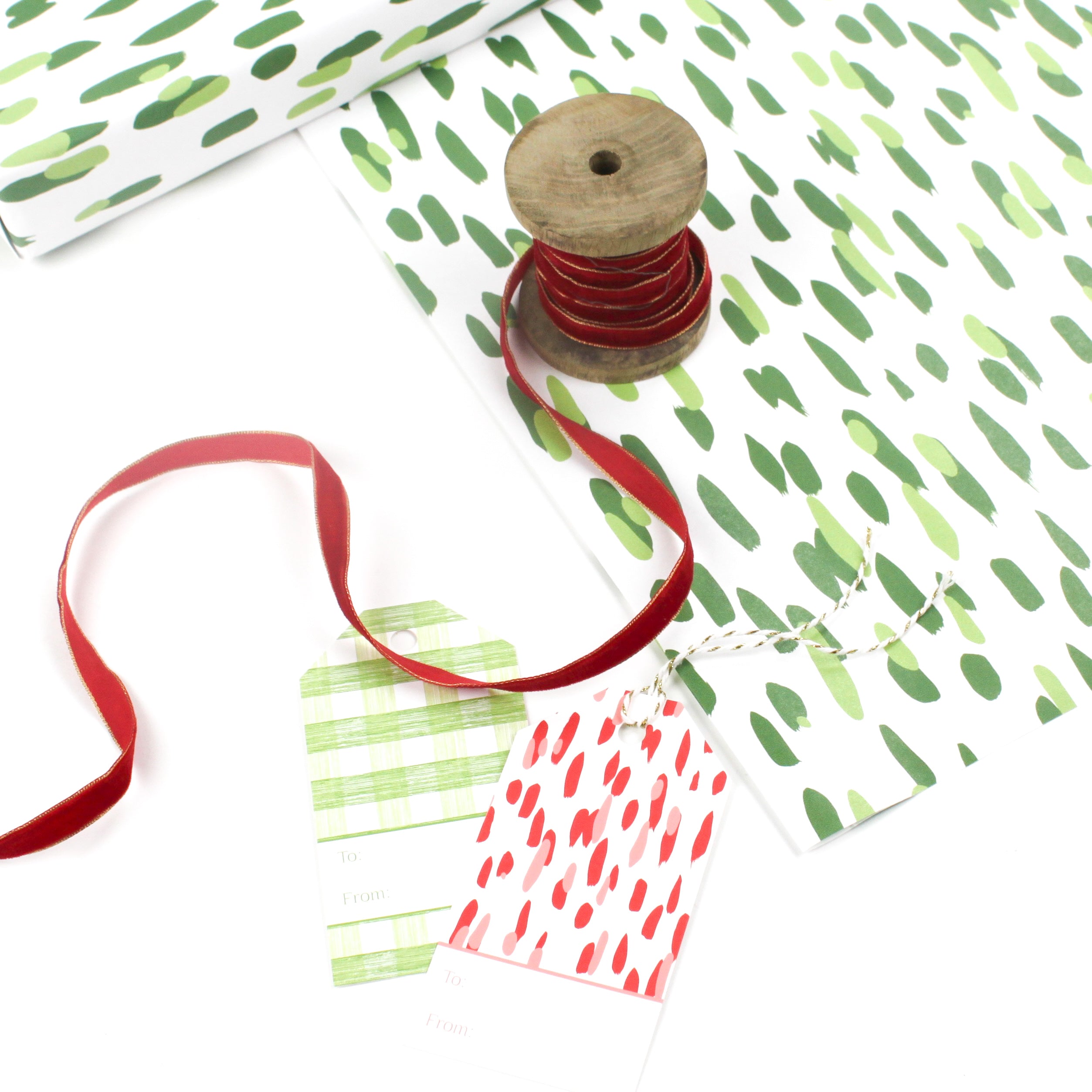 Styled display of green brushstroke wrapping paper with gift tags and red ribbon.