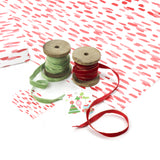 Styled display of red brushstroke wrapping paper with ribbons and holiday gift tags.